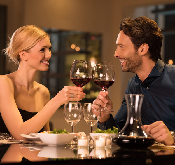 Romantic young couple at restaurant raising a toast. Beautiful couple with glasses of red wine in restaurant. Couple toasting wine glasses during a romantic dinner in a gourmet restaurant.